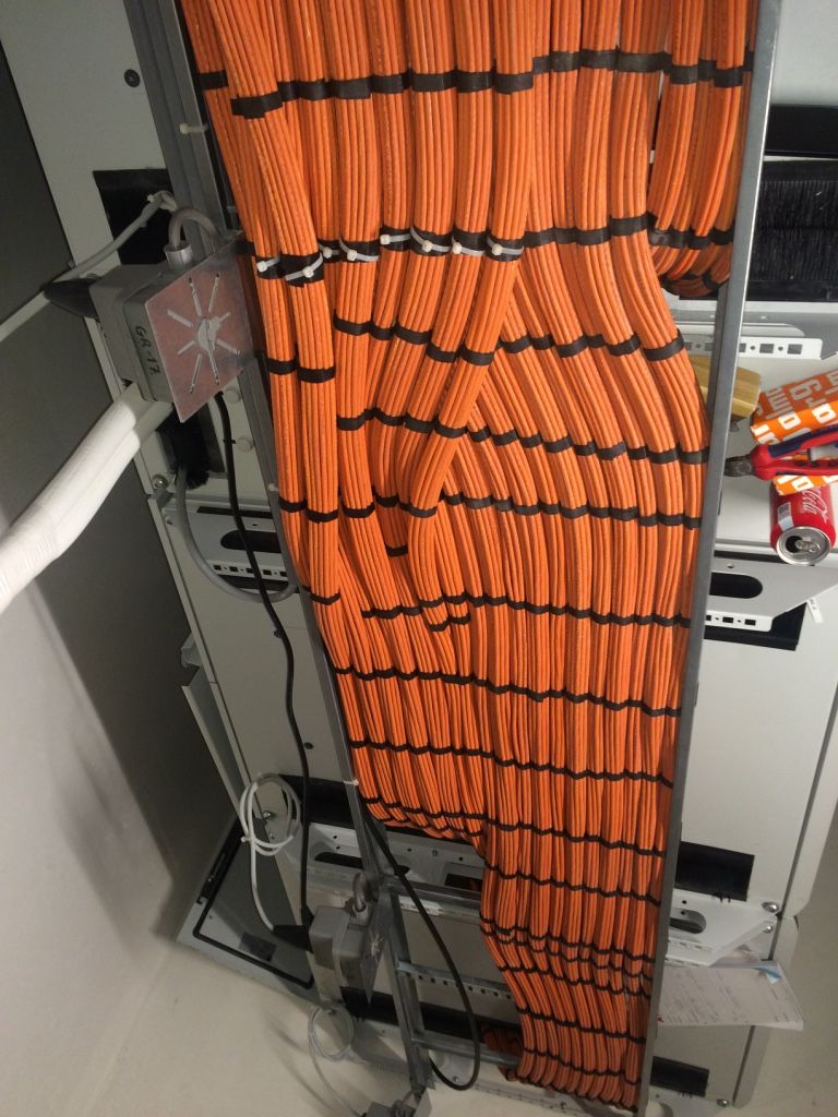 Orange data cables routed from a ceiling tray into an open rack